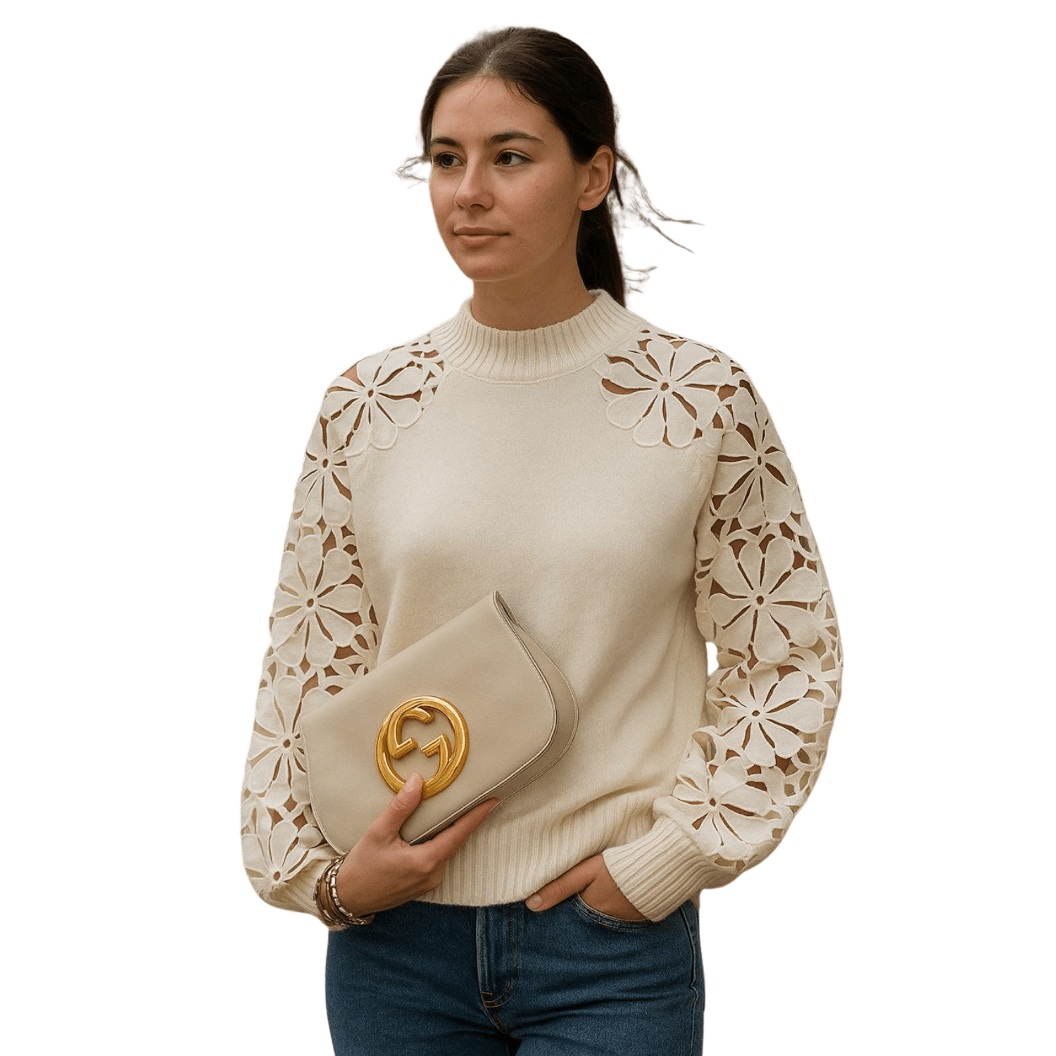 Woman wearing a cream sweater with floral lace sleeves, holding a beige clutch, styled with blue jeans