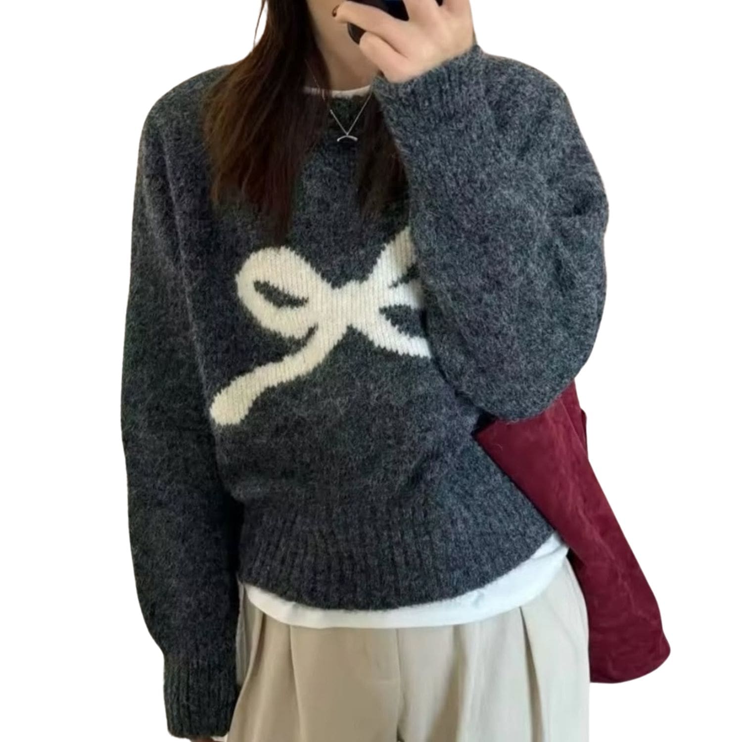Woman wearing a dark grey knit sweater with a large white bow design on the front