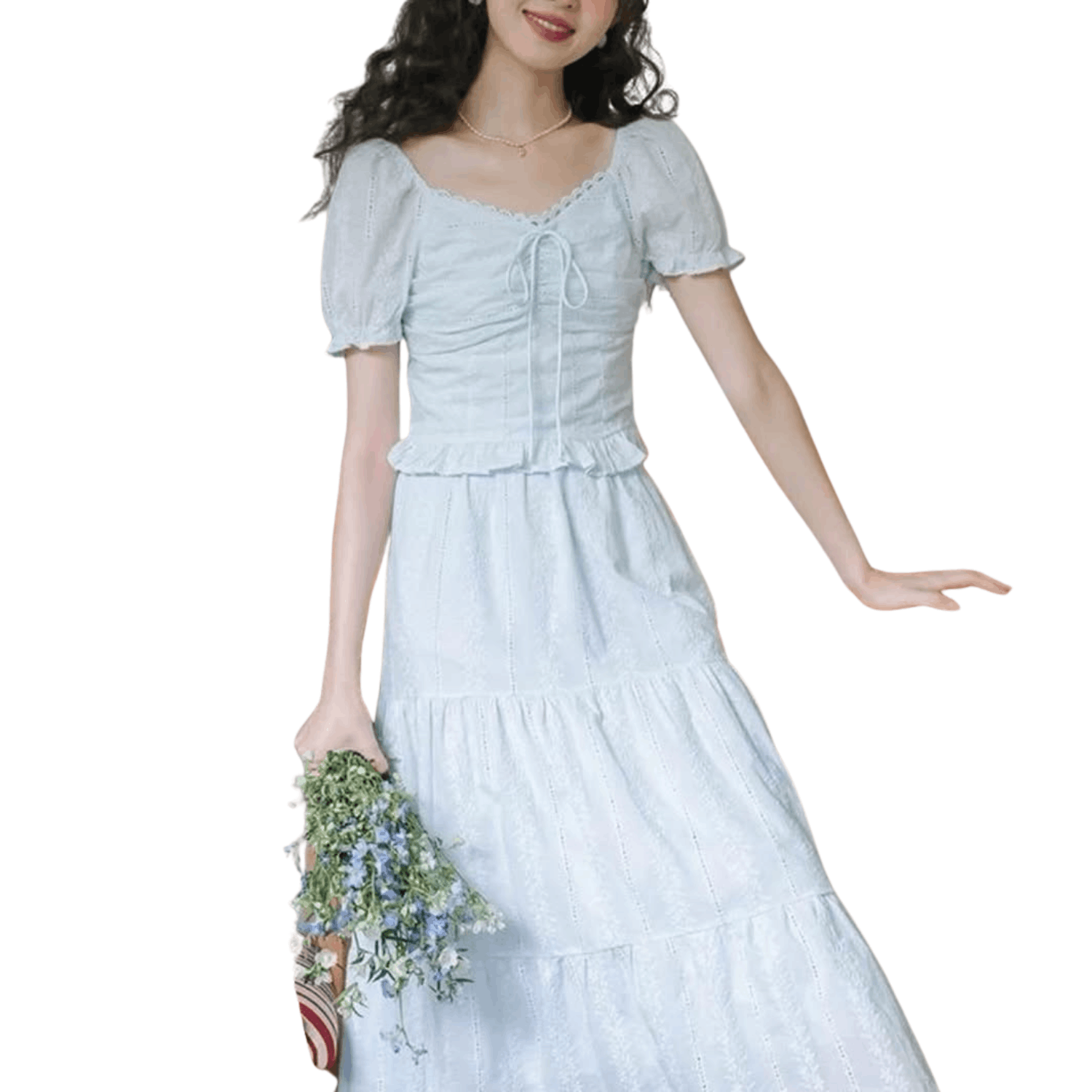 Woman wearing a white eyelet lace two piece set with puff sleeve tie front top and tiered midi skirt holding flowers